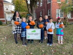 Smiling students and teacher pose with pumpkins and "This School Supports Kentucky Farmers" sign