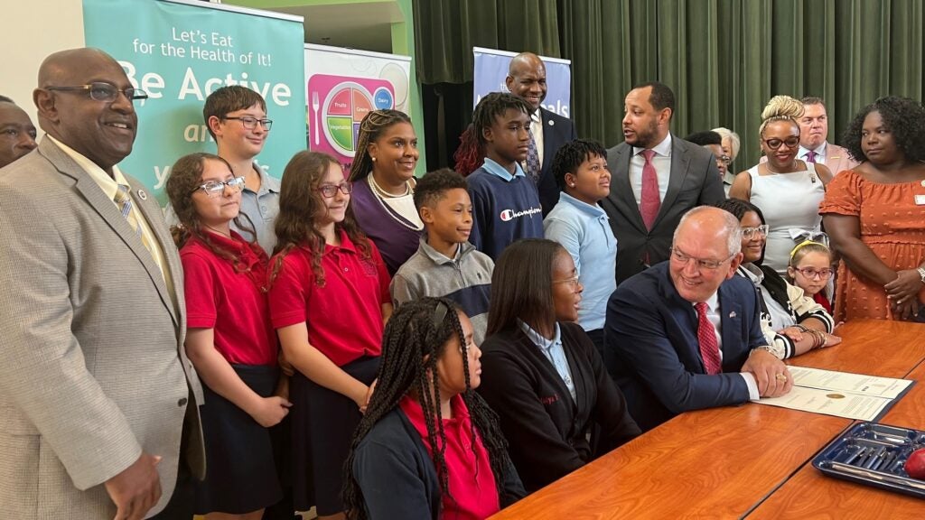 Governor Edwards sits at his desk, surrounded by students and advocates