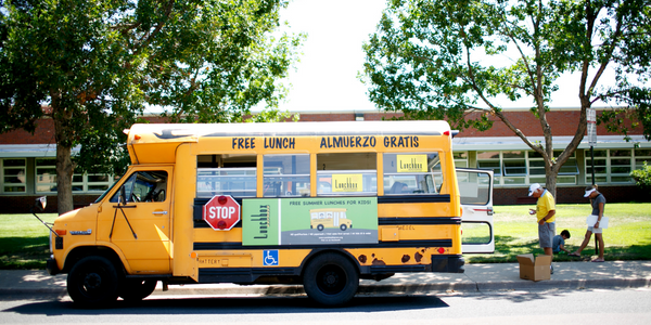 Short school bus is covered in signs saying Free Meals Here in English and Spanish