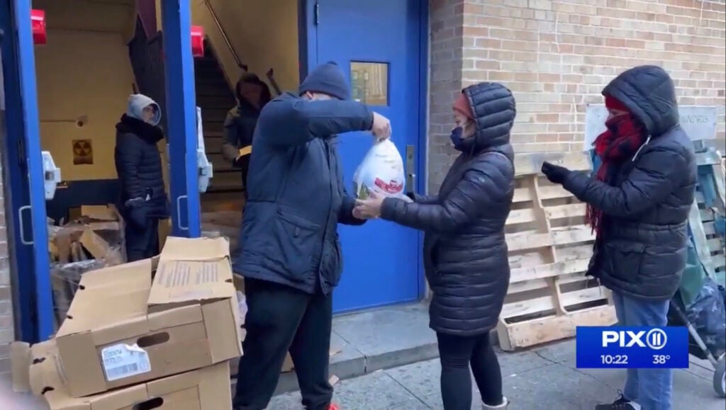 A food pantry volunteer hands a Thanksgiving turkey to community members in Washington Heights