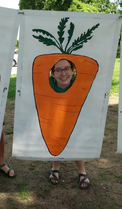 Claire's smiling face peeks through a cut out in a carrot decoration.