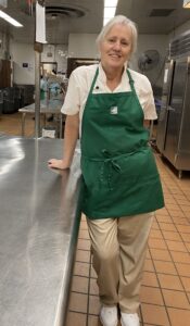 Frances, wearing her uniform, leans against a work table and smiles at the camera