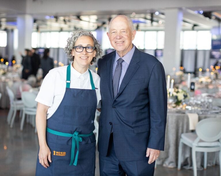 Chef Co-Chair Hillary Sterling, wearing an apron, wraps her arm around Share Our Strength Founder Billy Shore, who wears a suit