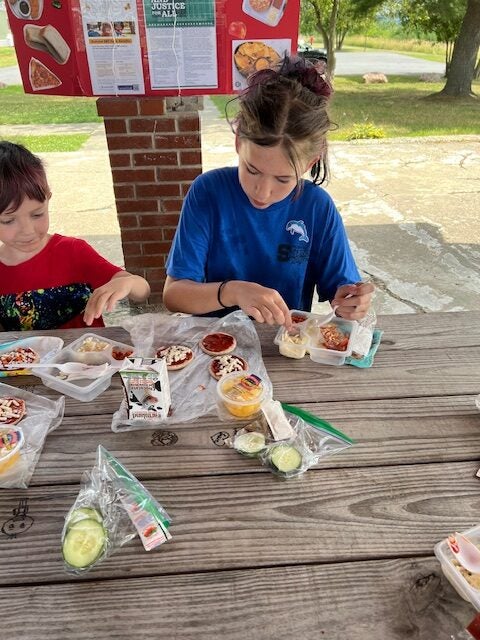 Two kids sit at a table and eat lunch