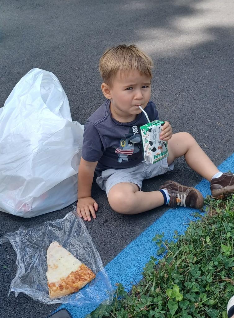 A young child sits on the ground, drinking from a juice box