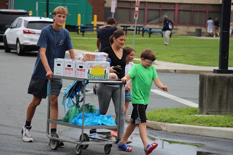 A volunteer helps a family wheel a cart with food boxes