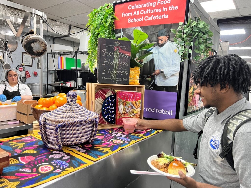 A student holds a plate of food and reaches out to grab a smoothie