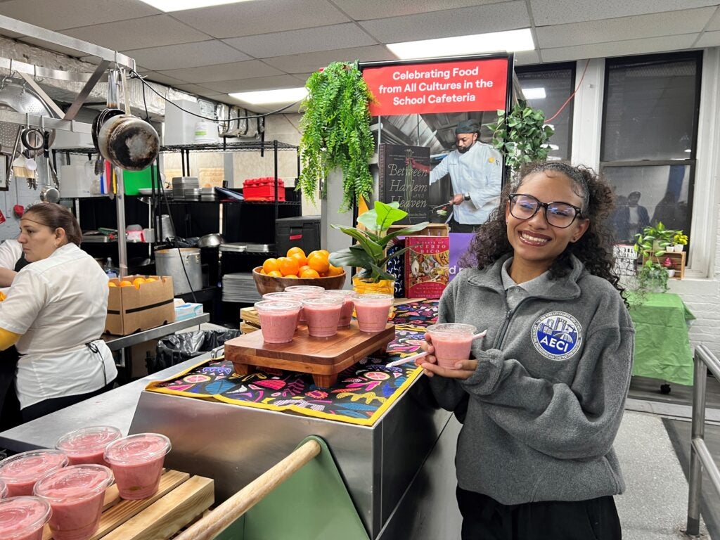 A student smiles at the camera, holding her smoothie