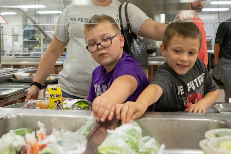 Two young boys reach to pick food from a serving station